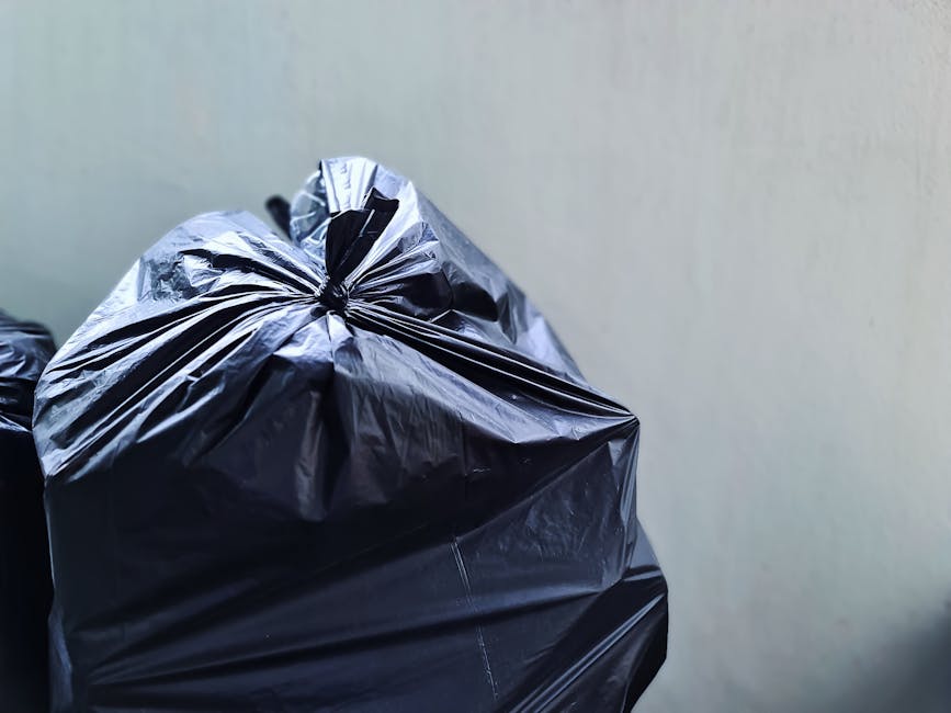 A row of large wheeled rubbish bins lined up alongside a brick wall on a pavement, with the green bin closest to the camera and the others in alternating colours of blue, red, and green extending into